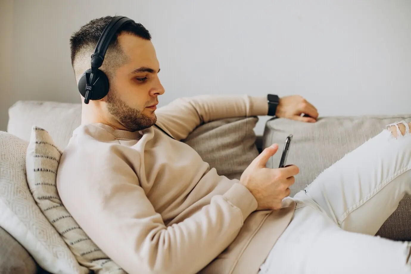 Молодой мужчина лежит на диване и слушает музыку в наушниках.